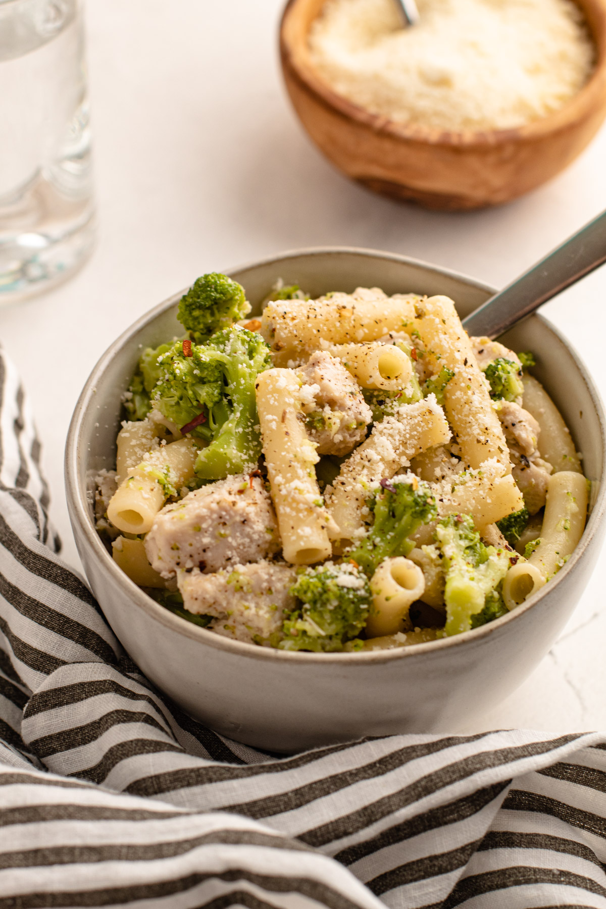 A bowl of chicken broccoli and ziti with parmesan cheese sprinkled on top.