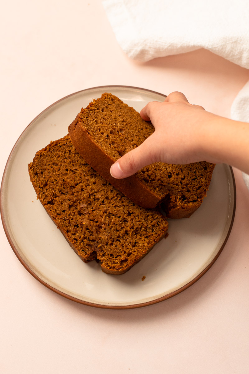 Two slices of whole wheat pumpkin bread on a plate being picked up.