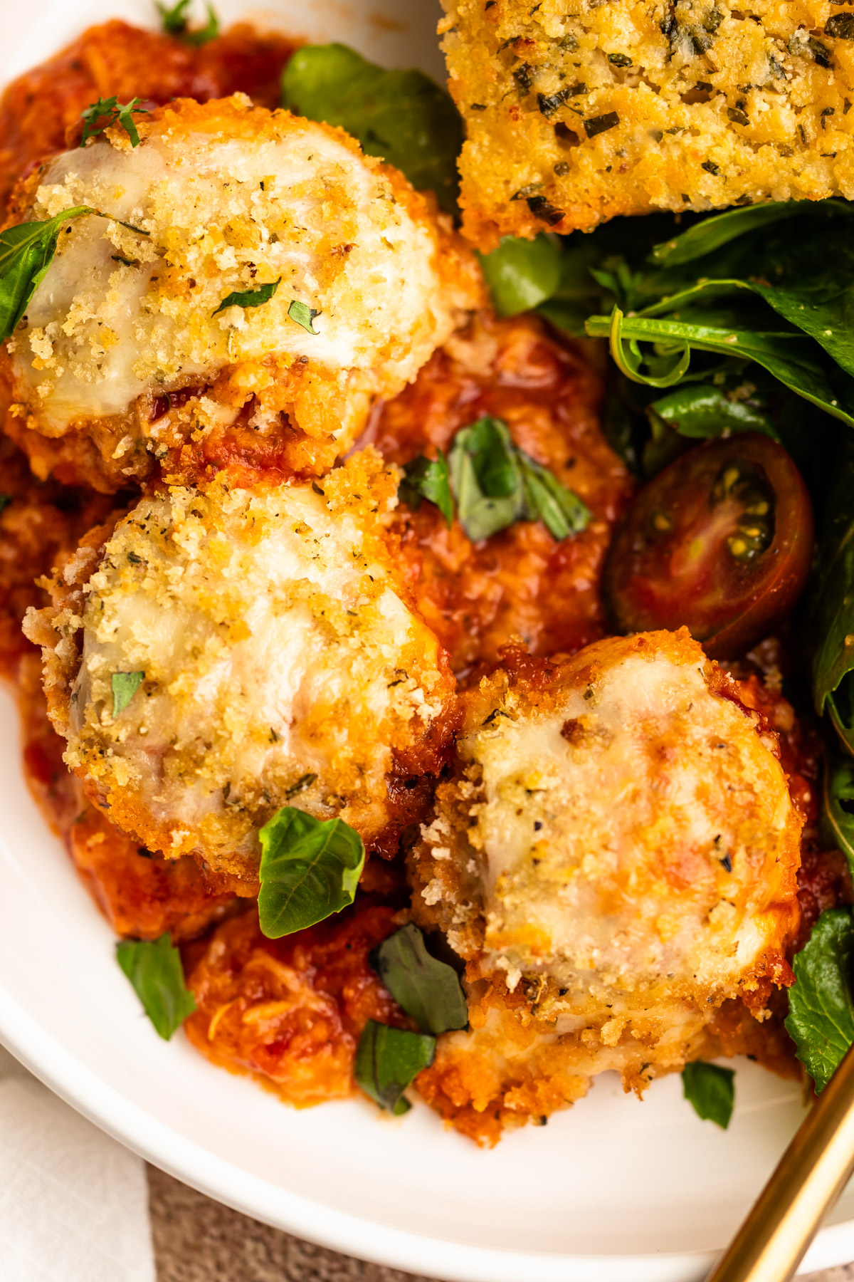 Chicken parmesan meatballs in a bowl with a salad and garlic bread.