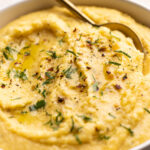 A bowl of creamy polenta with herbs and spices on top.