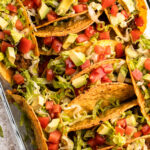 Oven tacos garnished with lettuce, tomato and avocado.