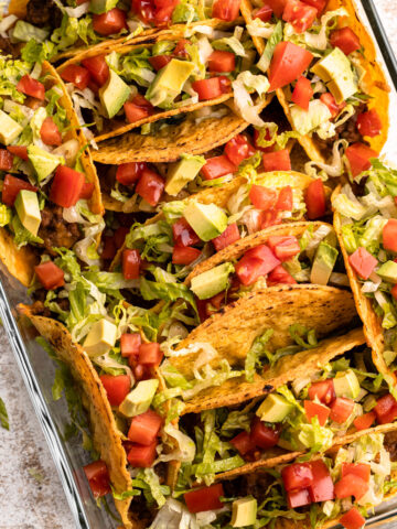 Oven tacos garnished with lettuce, tomato and avocado.