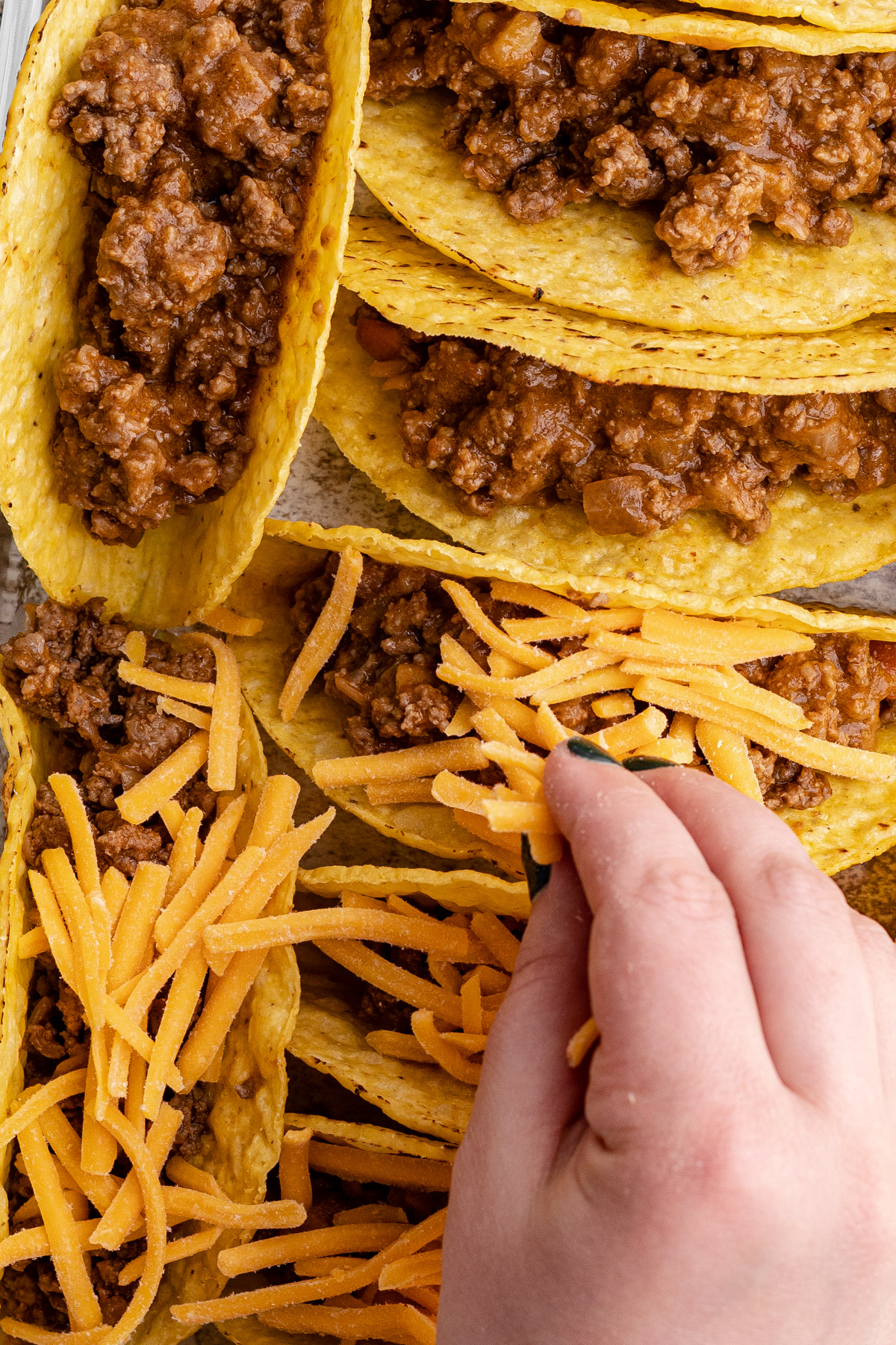 Placing cheese on taco filling to be baked in the oven.