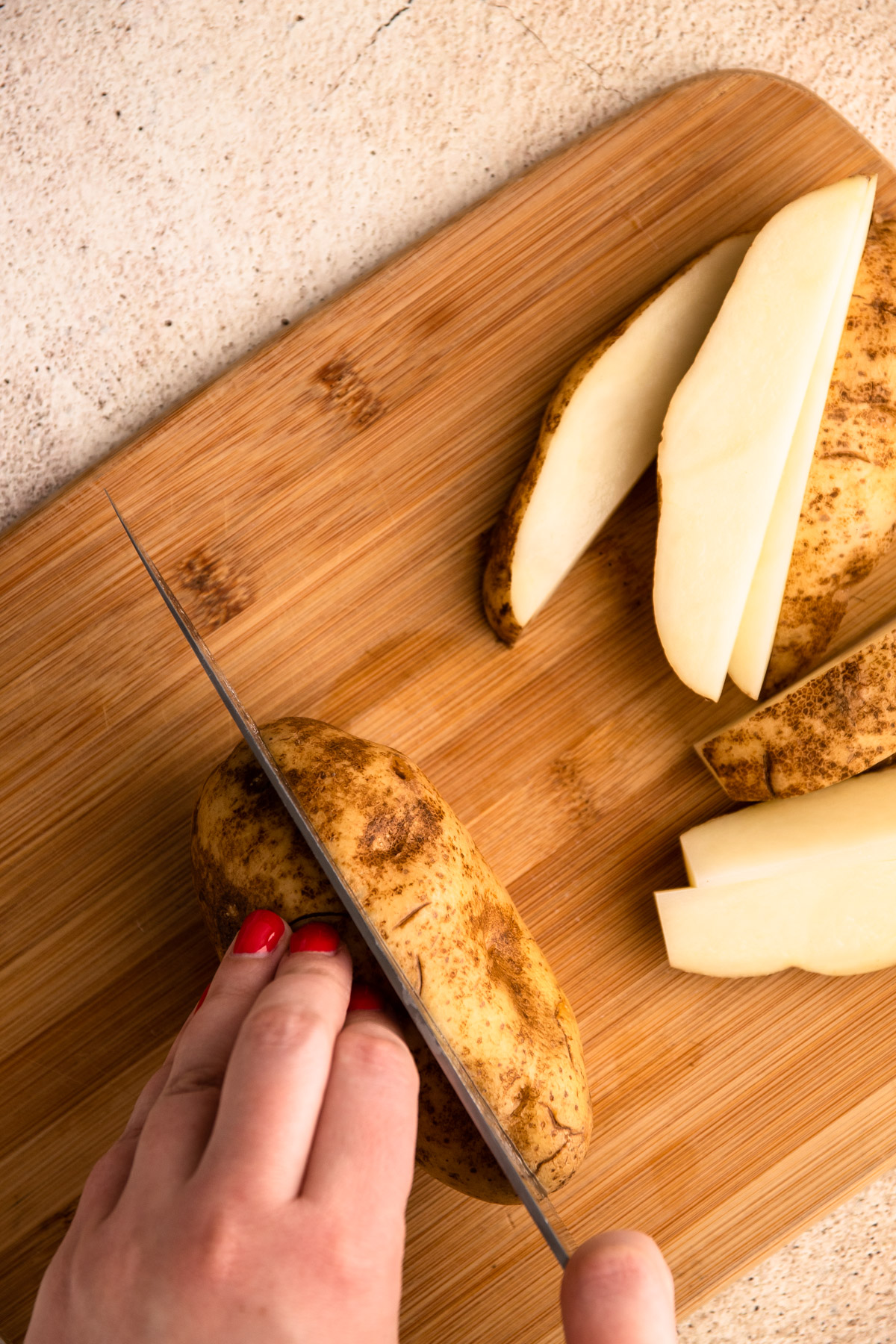 Russet potatoes on a cutting board being safely cut into wedges.