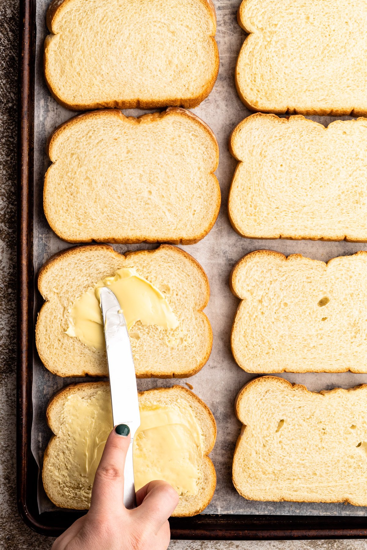 Putting butter on bread on a sheet pan for grilled cheese.