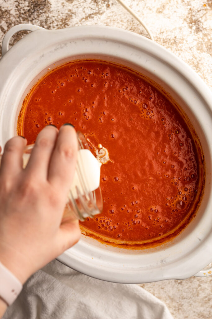 Tomato soup in a slow cooker with cream being proured in.