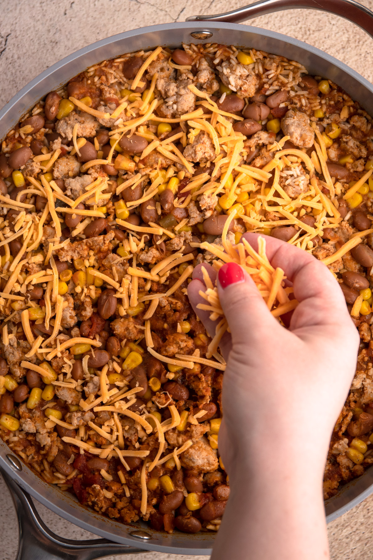 Putting cheese on ground turkey and rice with taco seasoning.