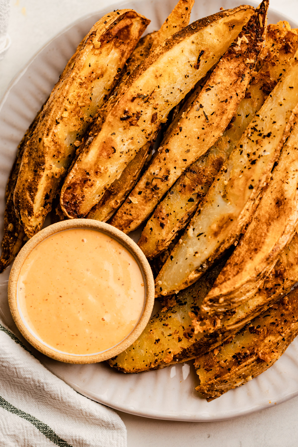 A plate of parmesan potato wedges baked in the oven with special sauce.