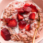 A bowl of strawberry oatmeal topped with fresh strawberries.