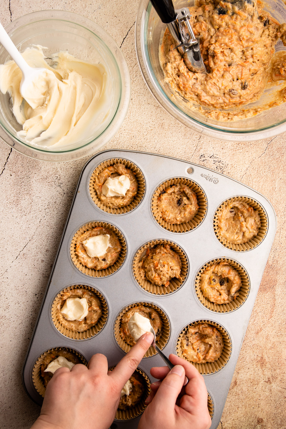 Placing cream cheese in the middle of carrot cake muffin batter.