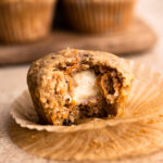 A baked carrot cake muffin with a bite taken to reveal a cream cheese center.