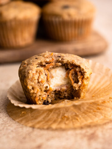 A baked carrot cake muffin with a bite taken to reveal a cream cheese center.