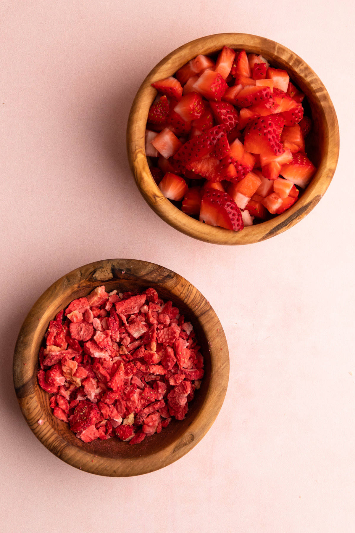 A bowl of fresh strawberries and a bowl of freeze-dried strawberries for strawberry muffins.