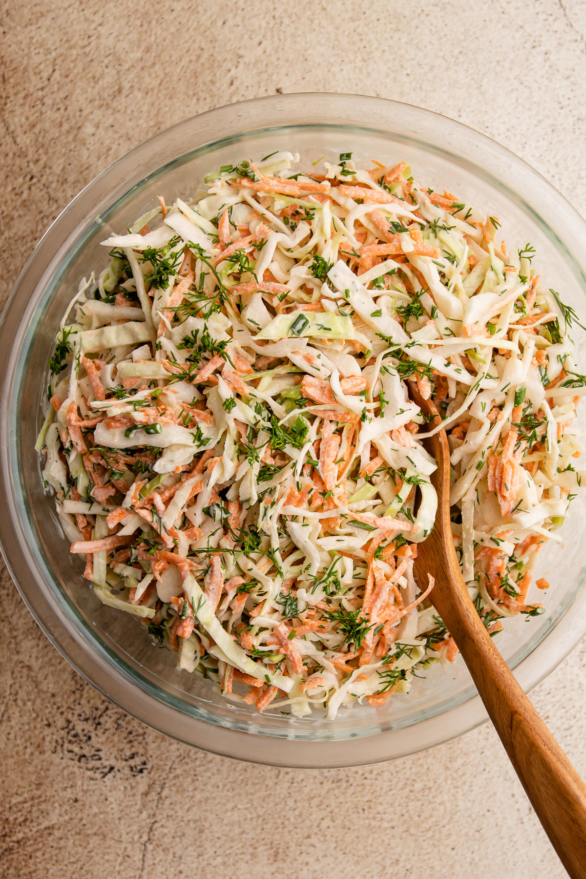 Coleslaw with dill in a bowl with a wooden spoon.