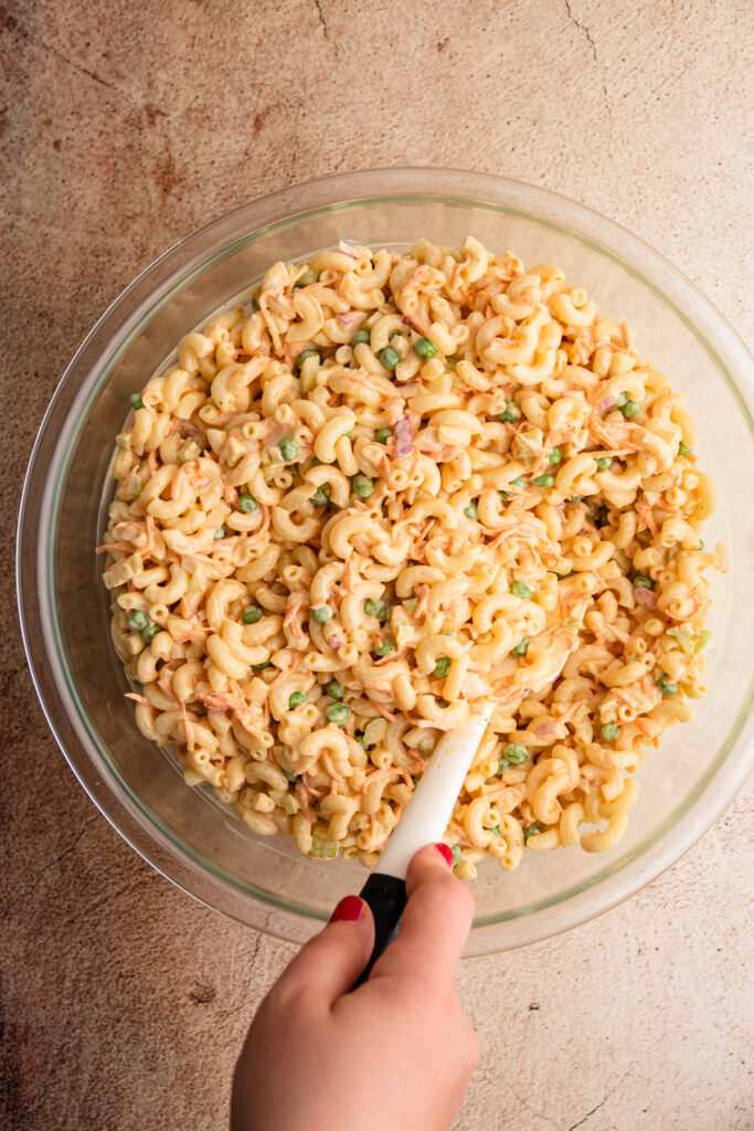 Macaroni salad in a bowl on a tan backdrop.