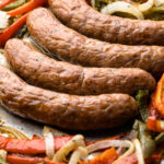 A sheetpan with baked sausage peppers and onions.