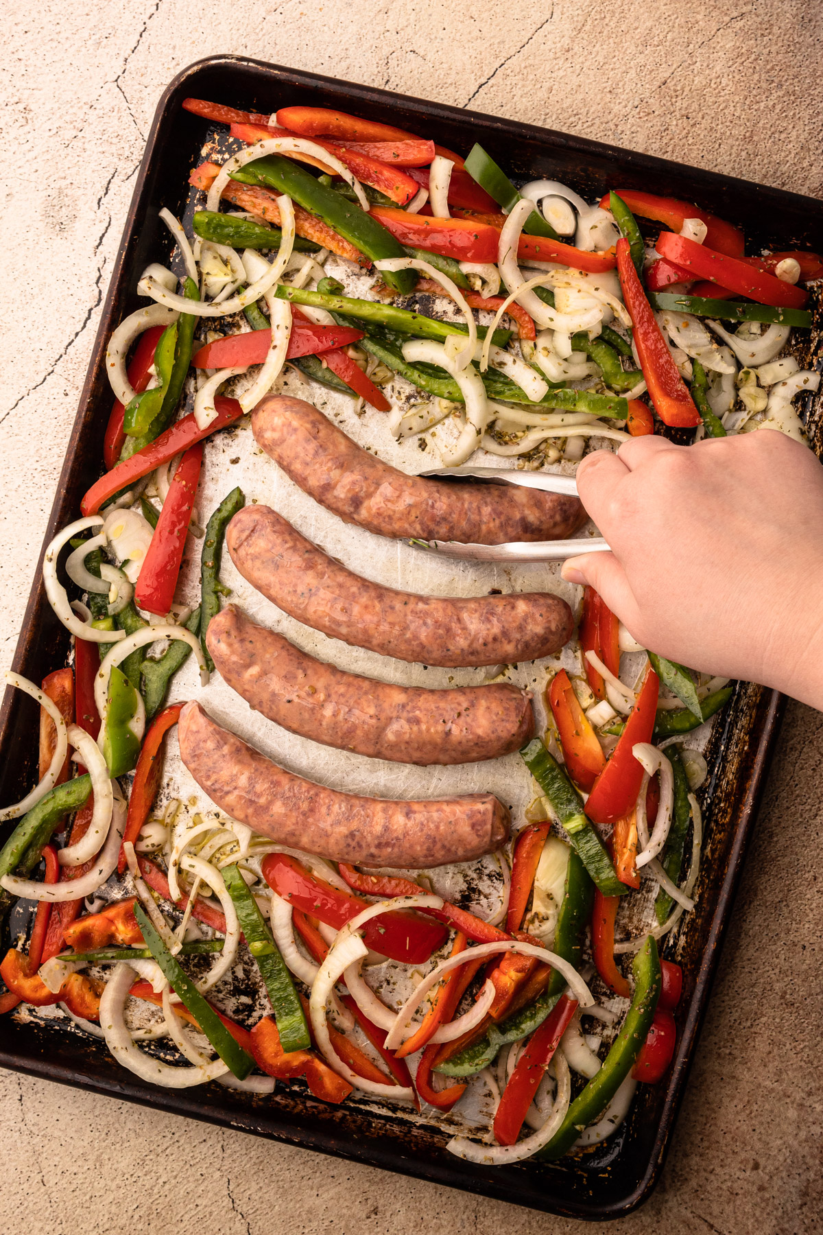 Sausage peppers and onions unbaked on a sheetpan.