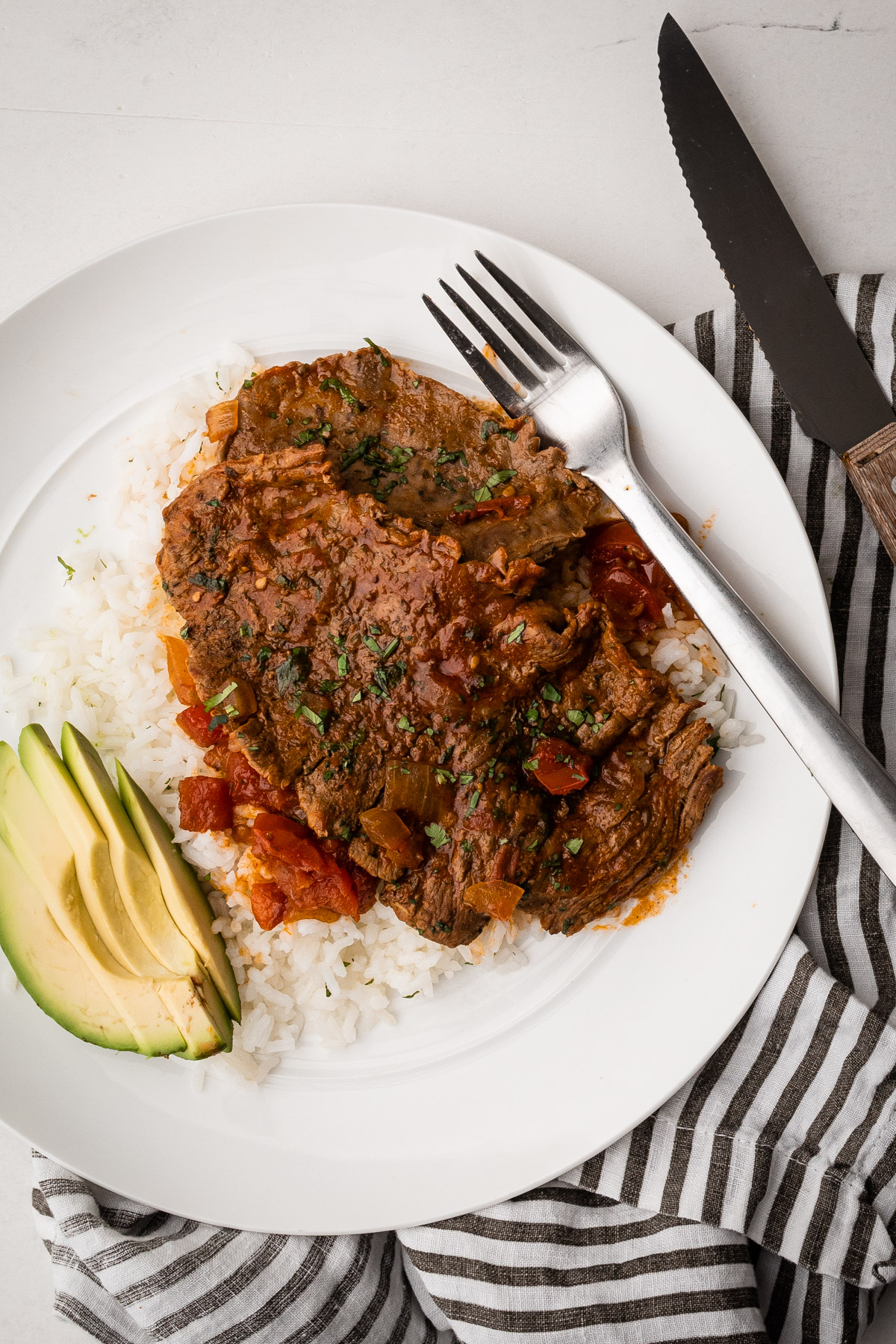 A plate of carne en bistec with avocado and rice.