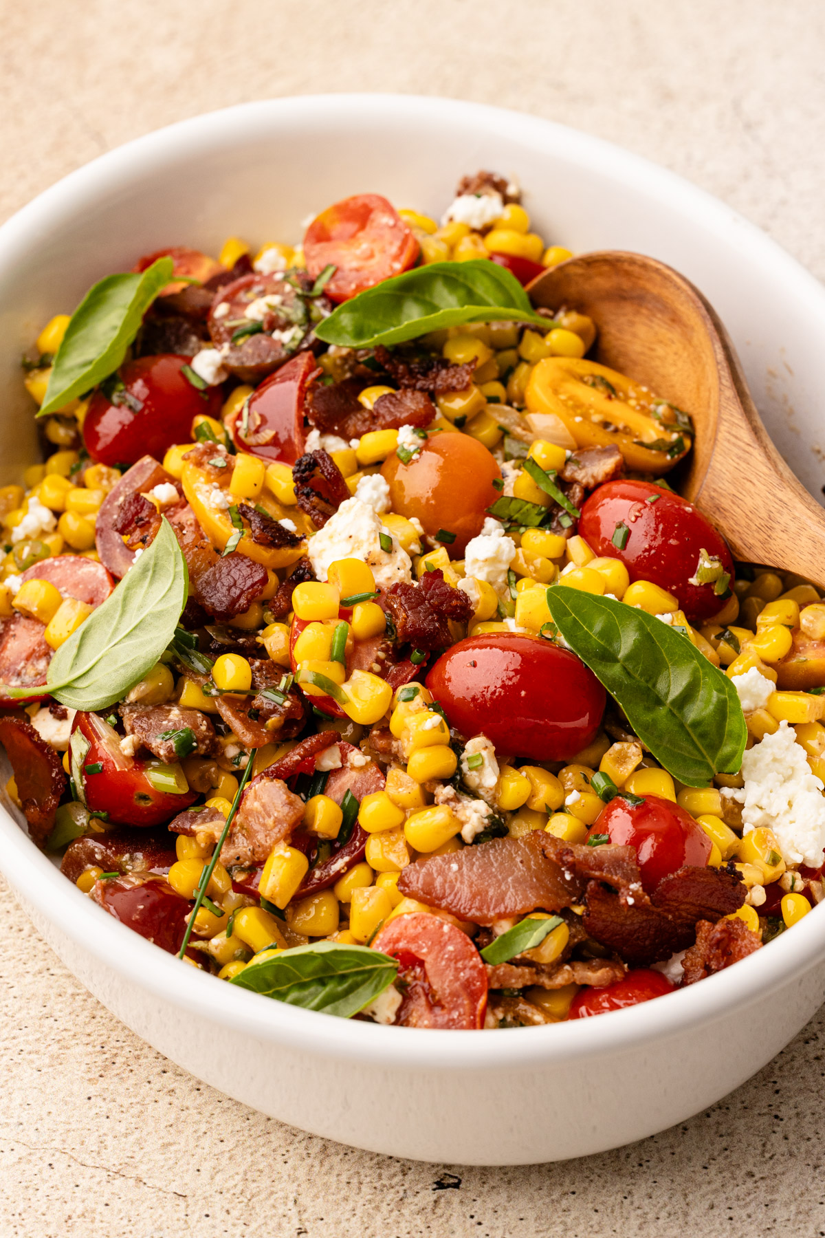 A serving platter of corn succotash with bacon and tomato and fresh herbs.