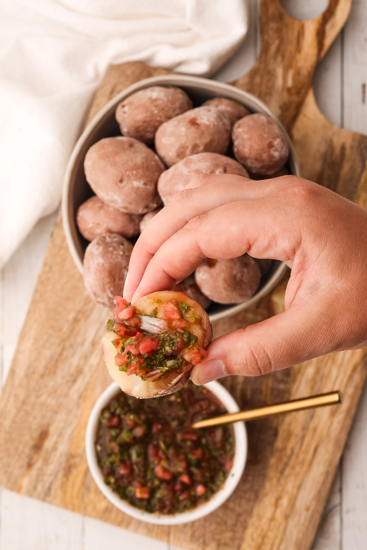 A salted potato being served with salsa on a wooden cutting board.