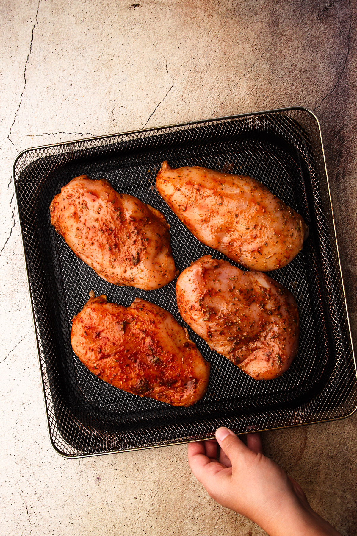 Four chicken breasts on the air fryer tray uncooked but with spices.