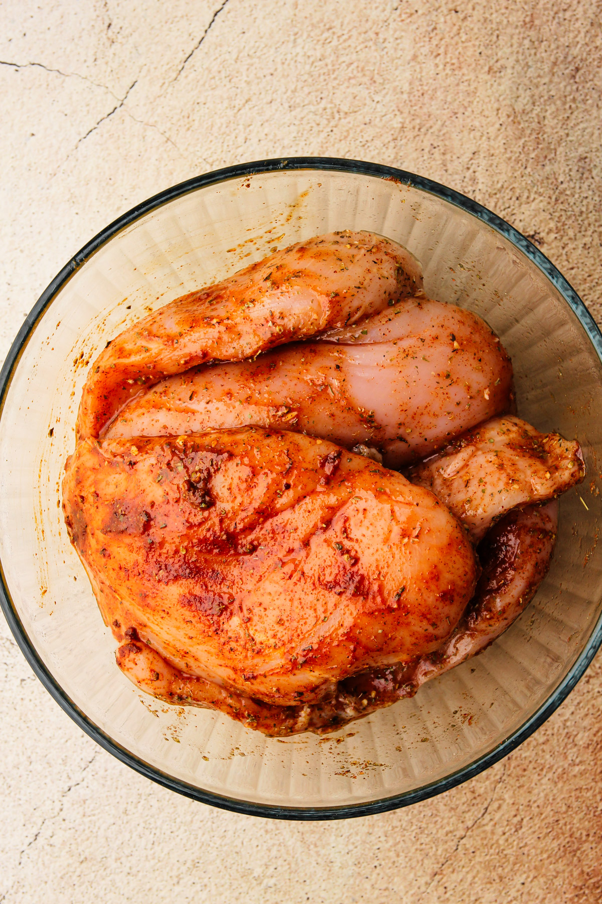 Chicken breasts in a bowl uncooked but with spices.