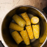 An instant pot insert filled with cooked corn on the cobb.