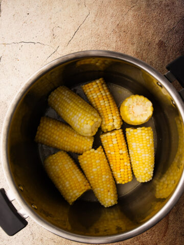 An instant pot insert filled with cooked corn on the cobb.