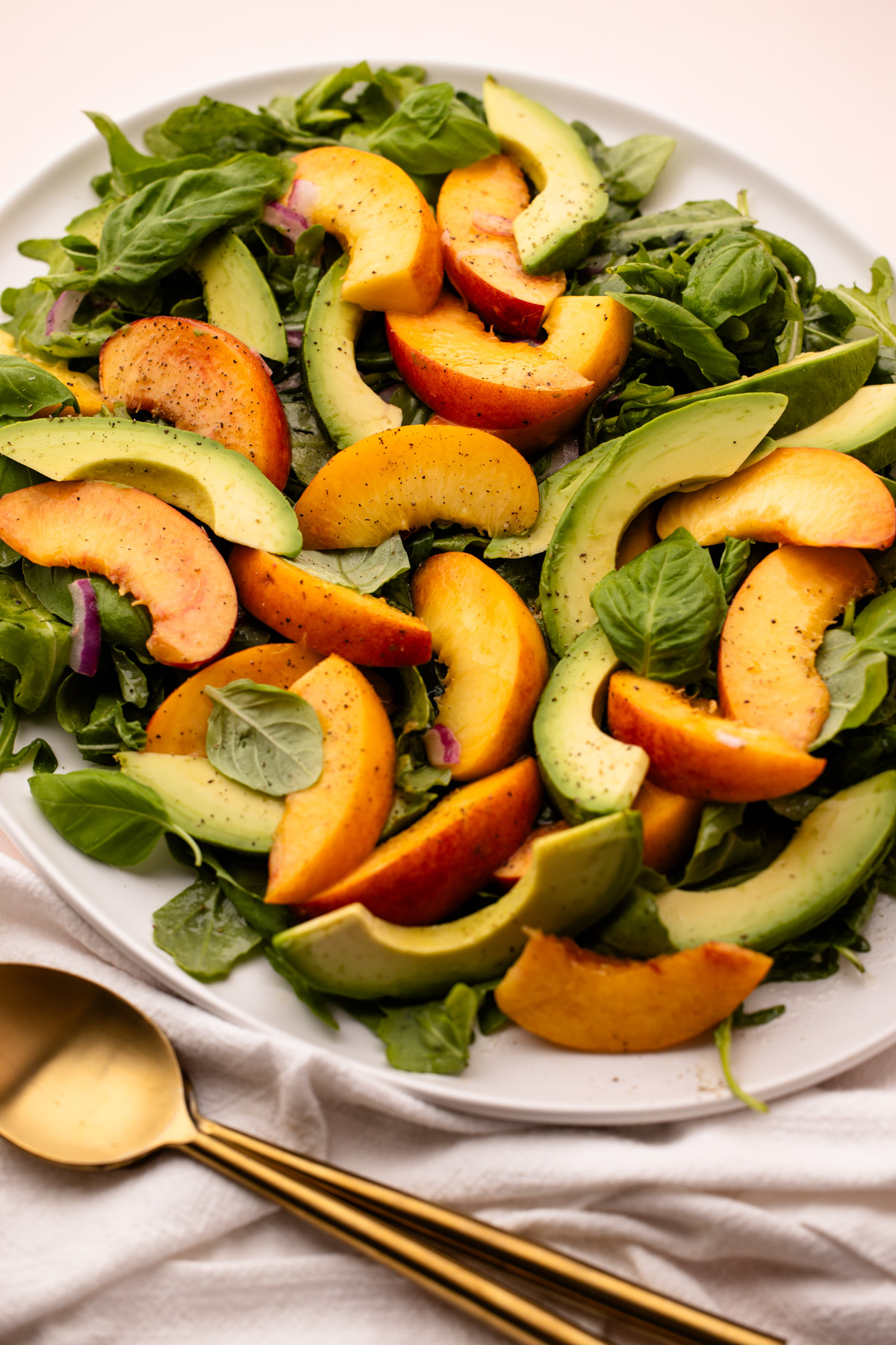 A platter with peach avocado salad with leaves of basil and arugula.