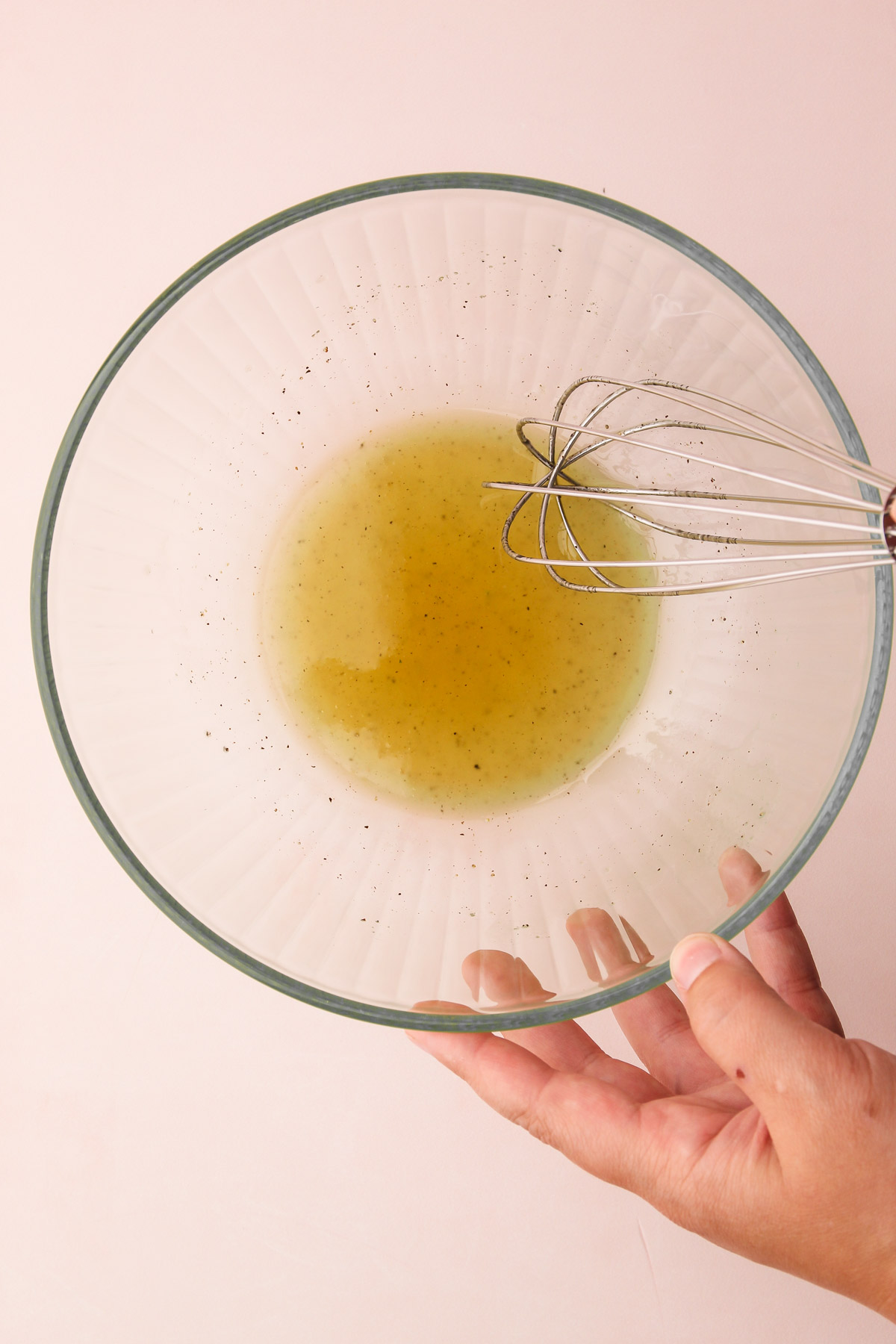 The dressing being prepared in a bowl on a pink background.