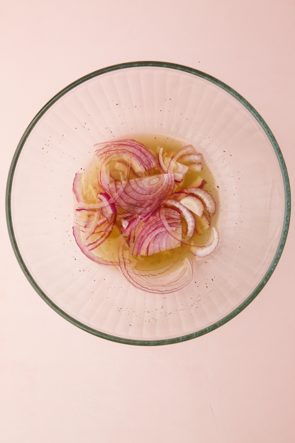 Thin sliced shallots macerating in the dressing in a bowl.