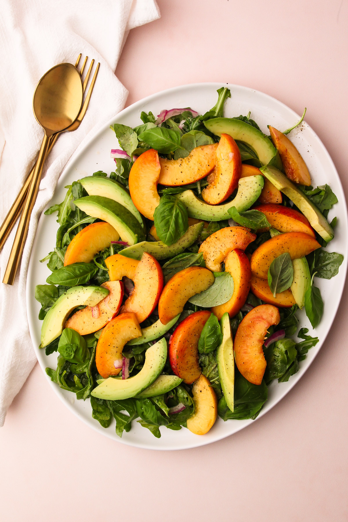 A platter with peach avocado salad with leaves of basil and arugula on a pink background.