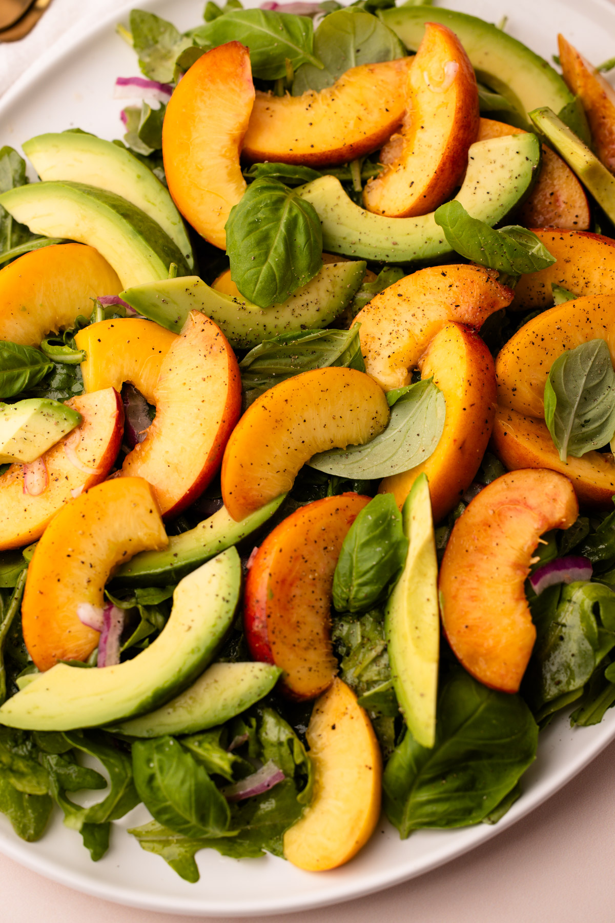 A platter with peaches, avocados, arugula scattered to make a salad.