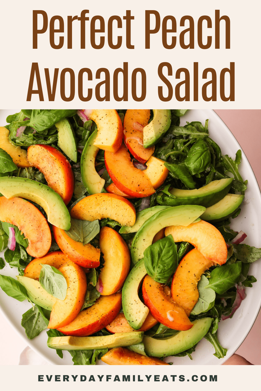 Peach and avocado salad with greens on a white plate with a pink background.