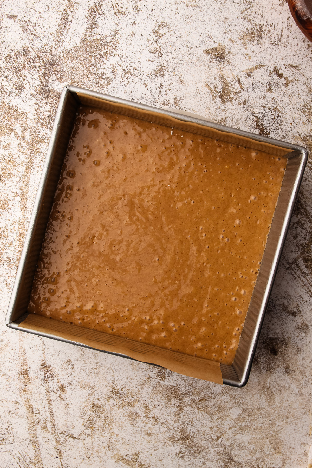 Brown, bubbly cake batter in a parchment-lined 8-inch square metal baking pan