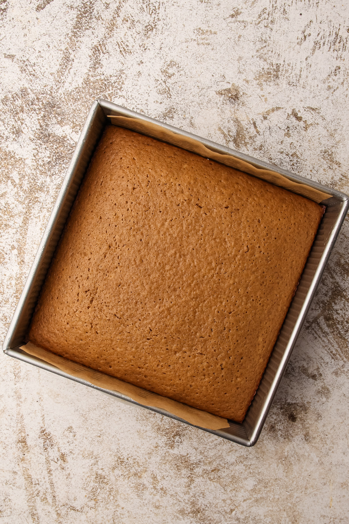 A fully baked cake in a parchment-lined 8-inch square metal baking pan.