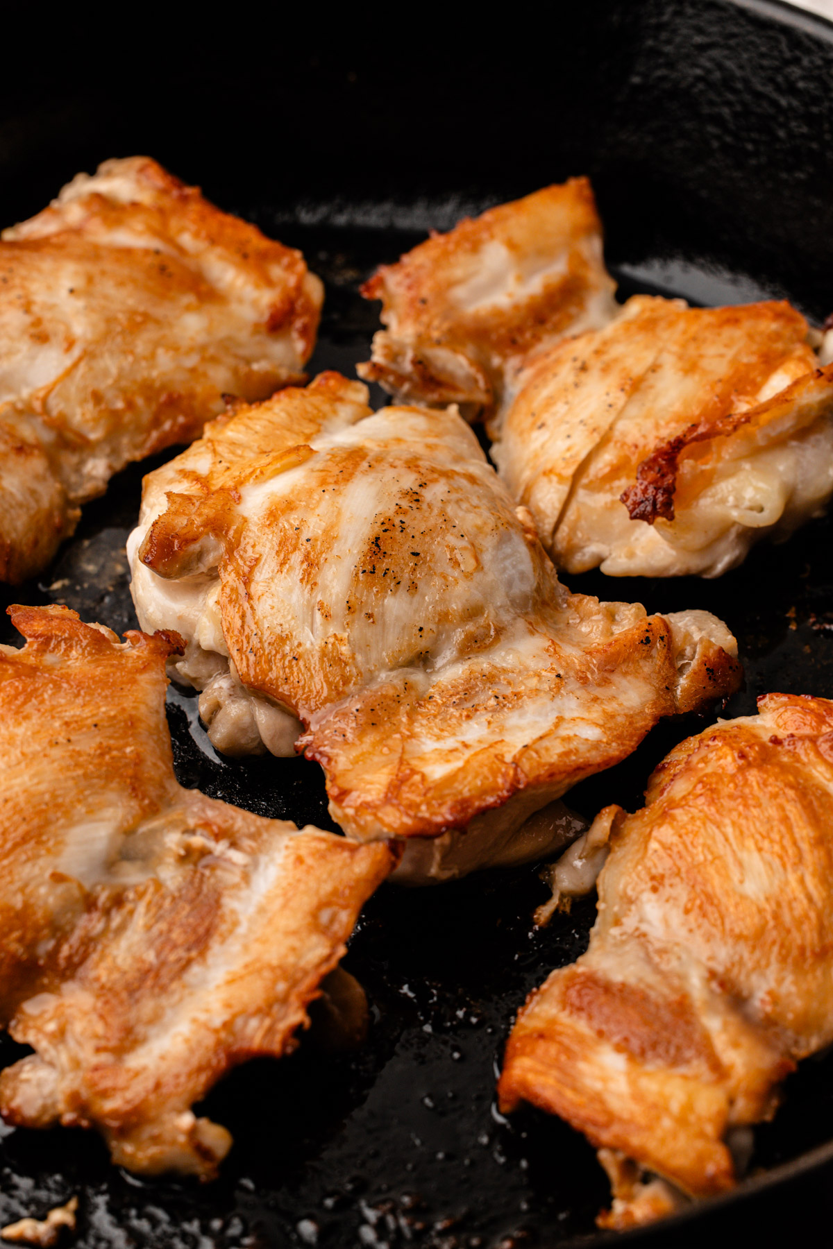 Chicken thighs seared and browned in a cast iron skillet.