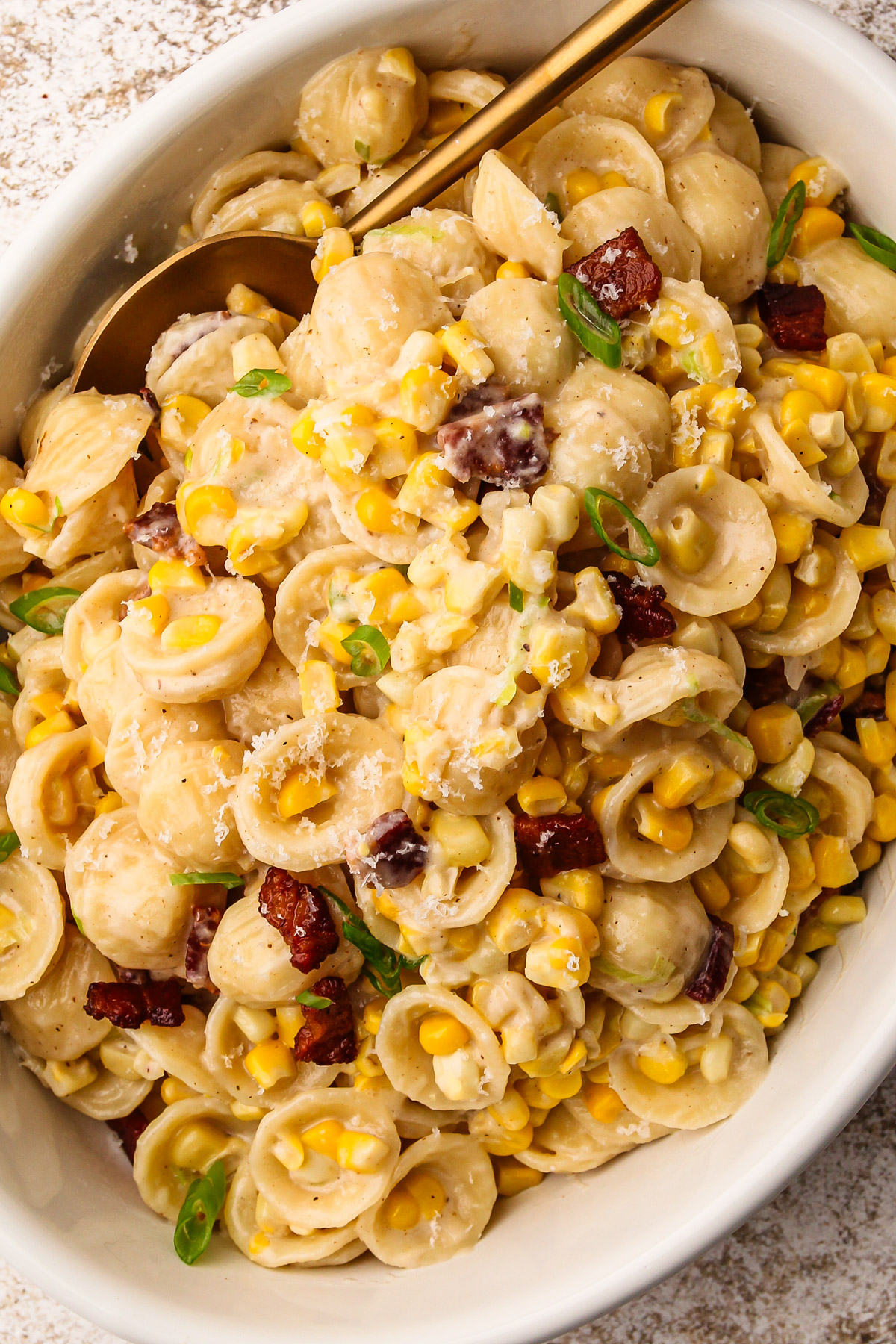 The finished corn pasta dish with bacon in a white serving platter with a gold spoon.