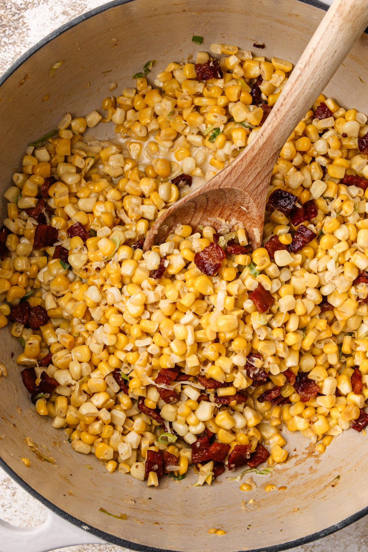 Corn and bacon cooking in a white dutch oven.