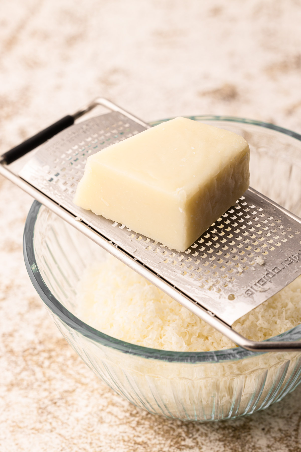 A block of cotija cheese on a microplane over a bowl.