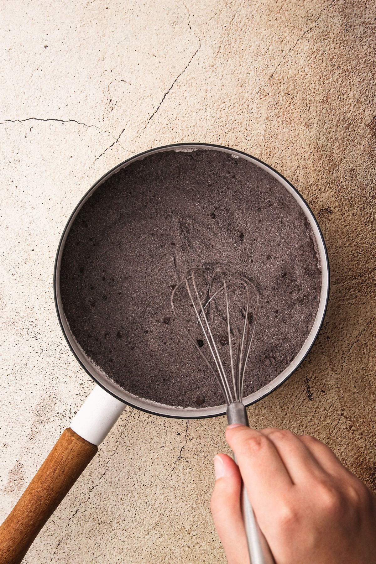 A hand whisking together a chocolate pudding mixture for Dirt Pudding Cups in a pot.