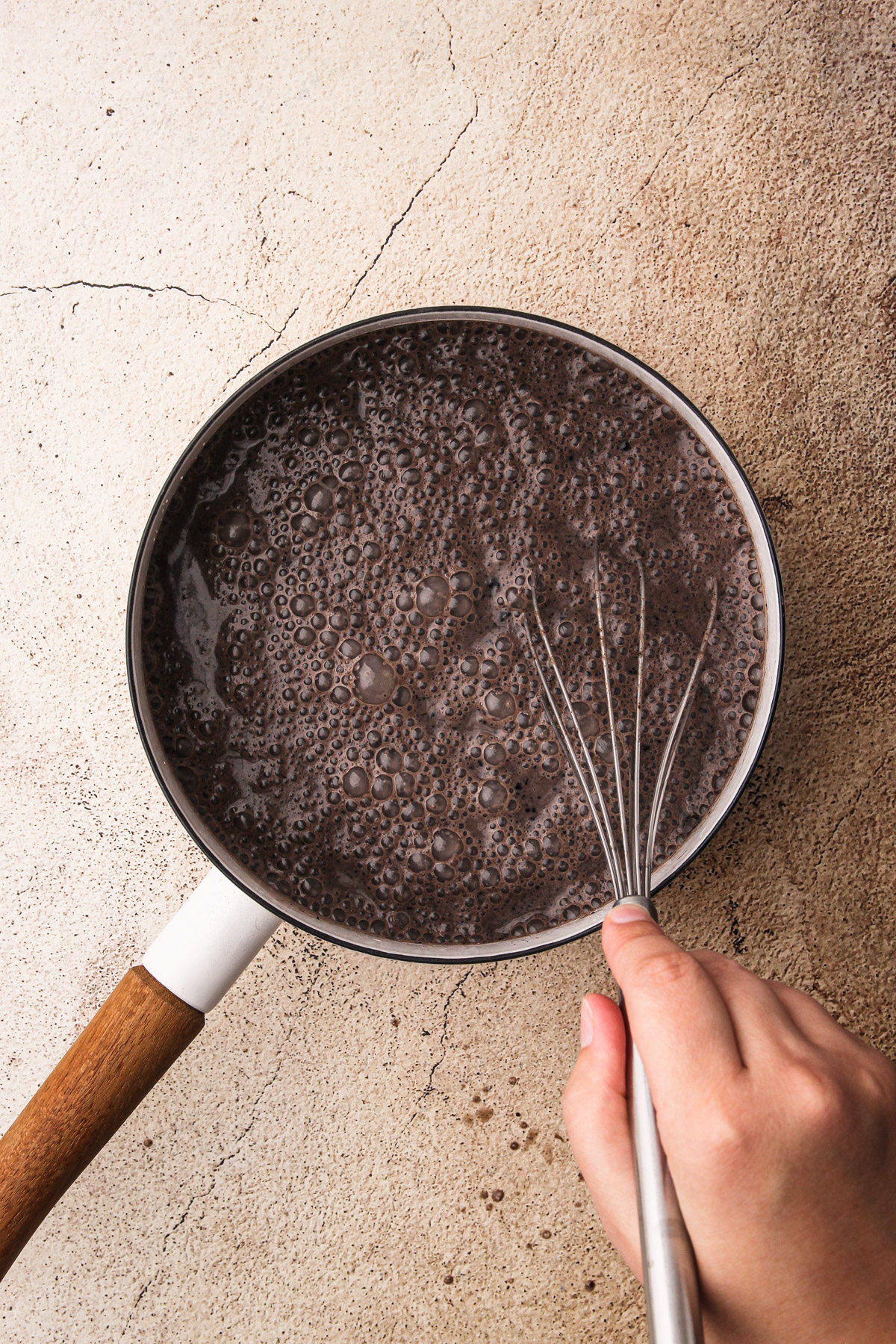 A hand whisking together a chocolate pudding mixture for Dirt Pudding Cups in a pot.