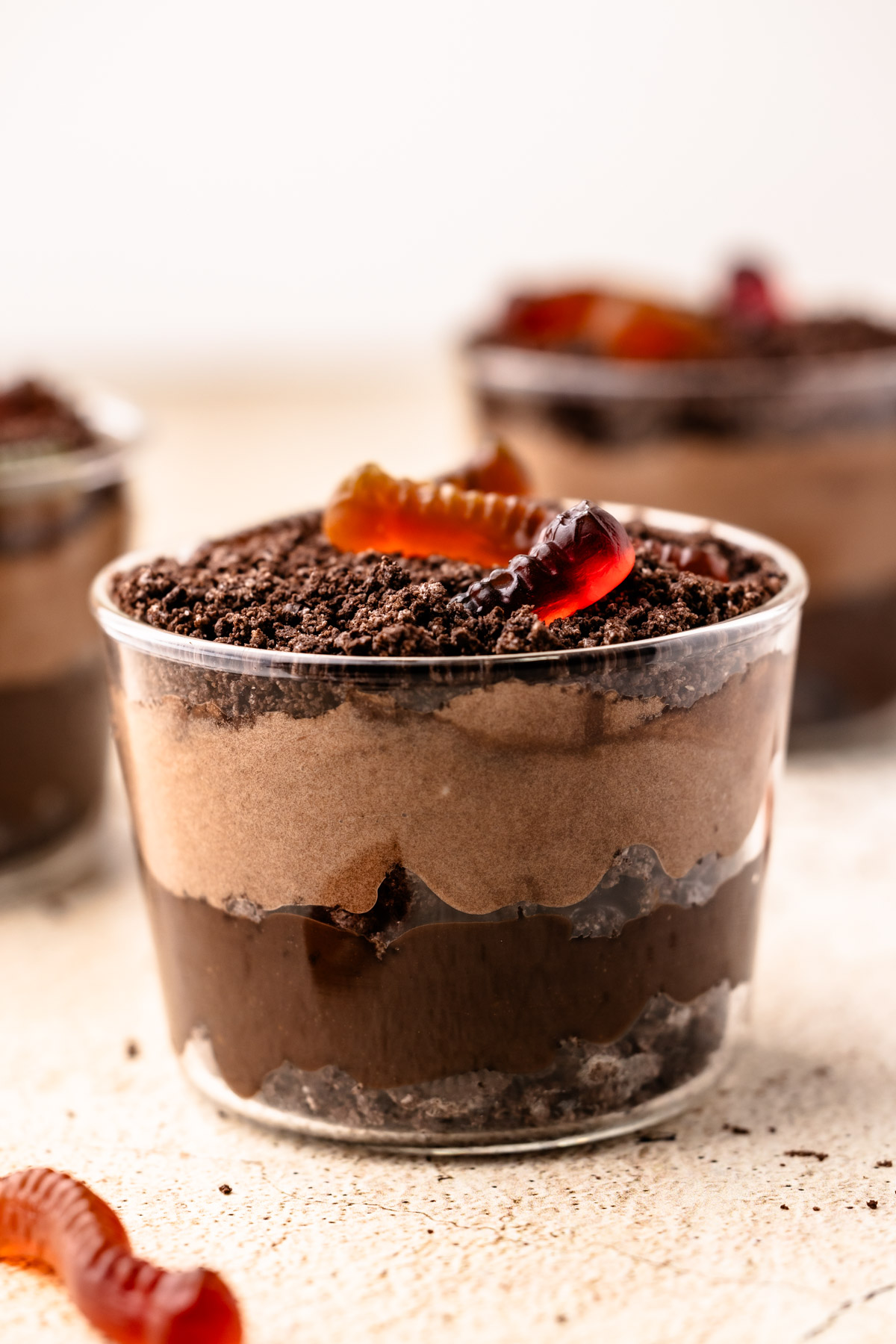 An assembled Dirt Pudding Cup in a glass with crushed cookies and gummy worms on top.