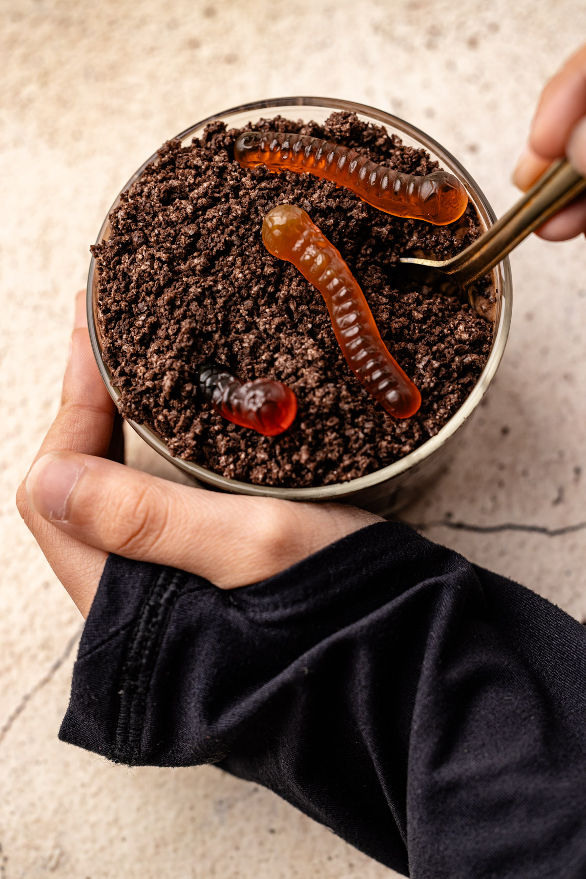 A hand holding a Dirt Pudding Cup and digging into the top with a spoon.