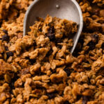 A metal scoop filled with maple walnut granola on a sheetpan.