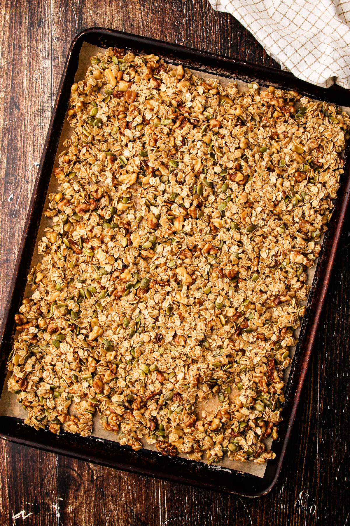 Unbaked maple walnut granola spread out into an even layer on a sheetpan.