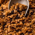 A metal scoop filled with maple walnut granola on a sheetpan.