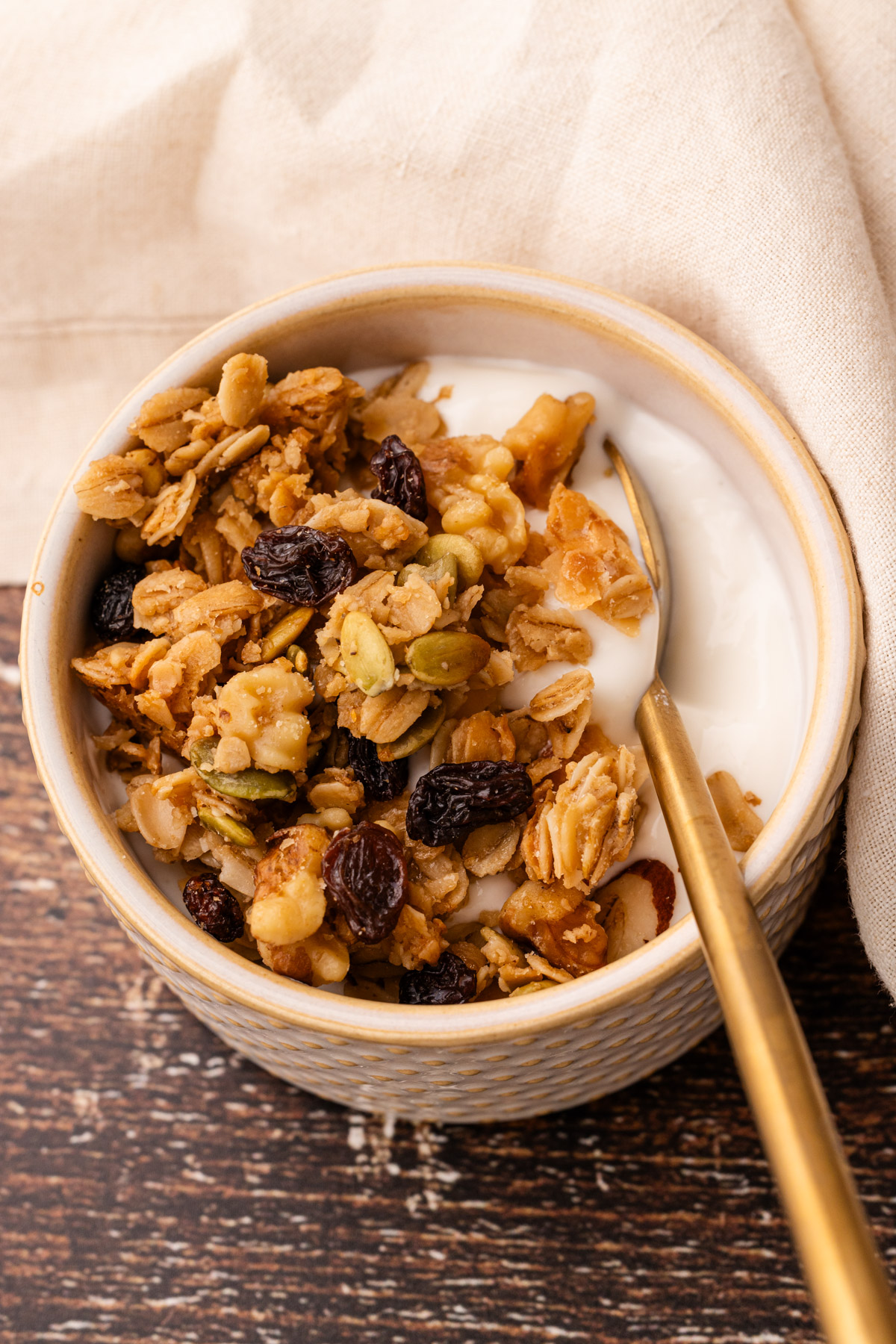 A bowl of yogurt with a spoon topped with maple walnut granola.