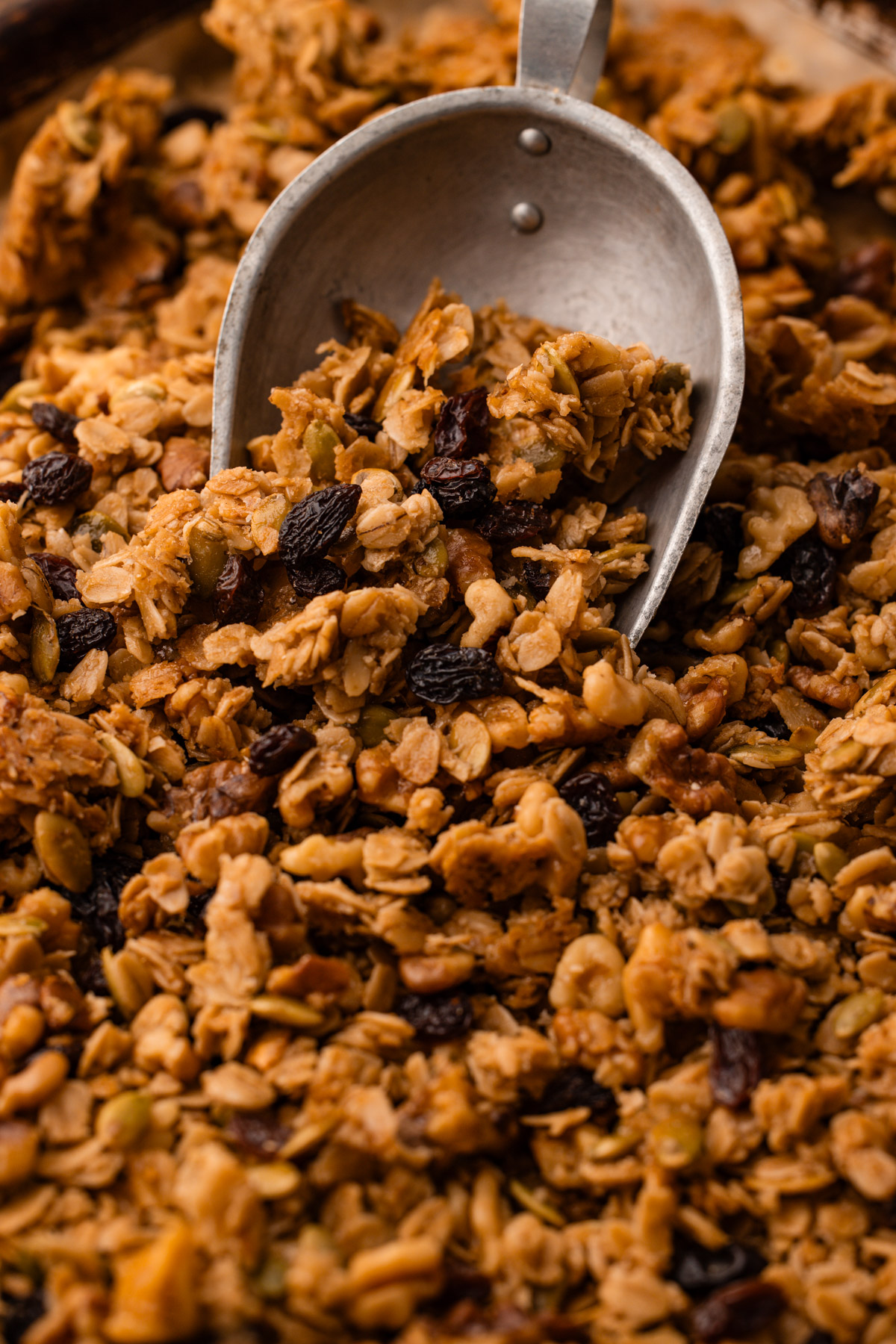 A metal scoop filled with maple walnut granola on a sheetpan.