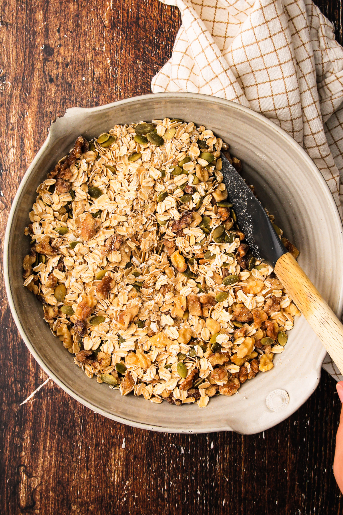 The dry ingredients for maple walnut granola mixed together in a bowl with a rubber spatula.